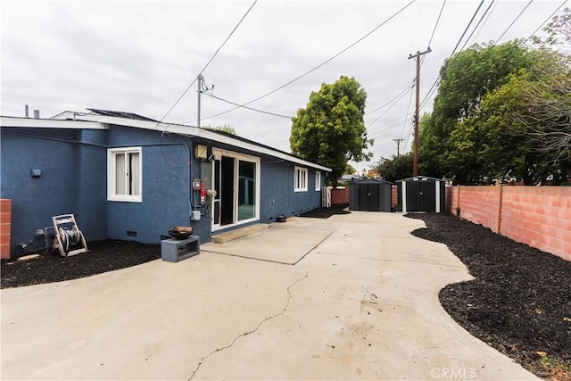 exterior space featuring a storage unit, a fenced backyard, stucco siding, and a patio area