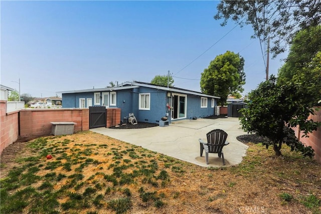 rear view of house featuring a patio, a gate, a storage shed, stucco siding, and a fenced backyard