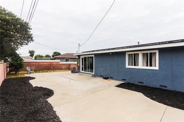 rear view of property with crawl space, stucco siding, a fenced backyard, and a patio area