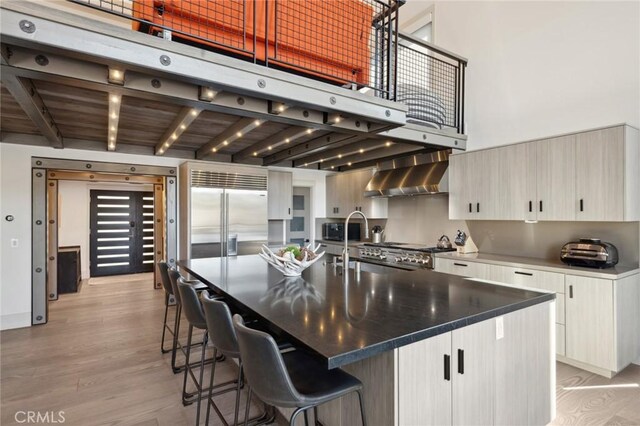 496 N State Highway 173, Lake Arrowhead, CA 92352 - kitchen with wall chimney range hood, stainless steel built in refrigerator, light wood-style flooring, a kitchen bar, and beam ceiling