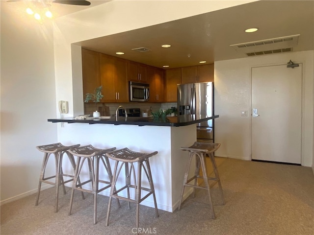 kitchen with a peninsula, dark countertops, a breakfast bar area, stainless steel appliances, and light colored carpet