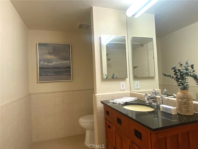 bathroom with visible vents, toilet, tile walls, vanity, and a wainscoted wall
