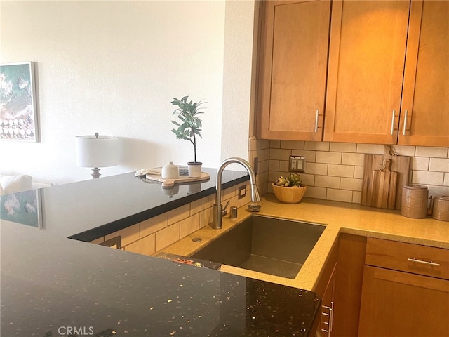 kitchen featuring brown cabinetry, decorative backsplash, a sink, and stone counters