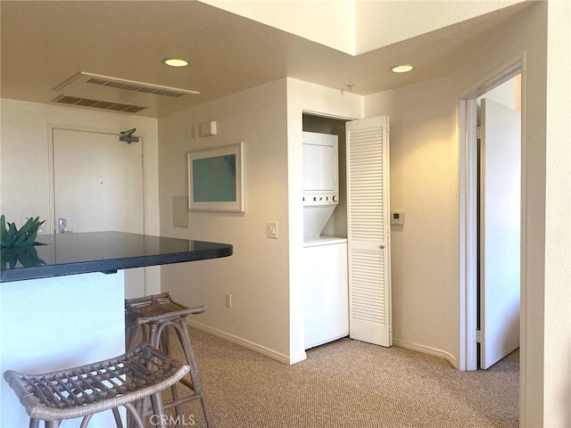 kitchen featuring baseboards, recessed lighting, stacked washer / dryer, and light carpet