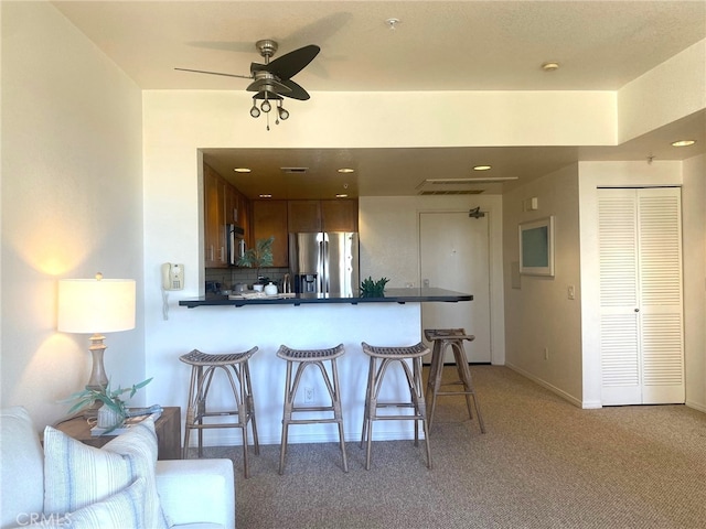 kitchen with stainless steel appliances, light carpet, a kitchen breakfast bar, and ceiling fan