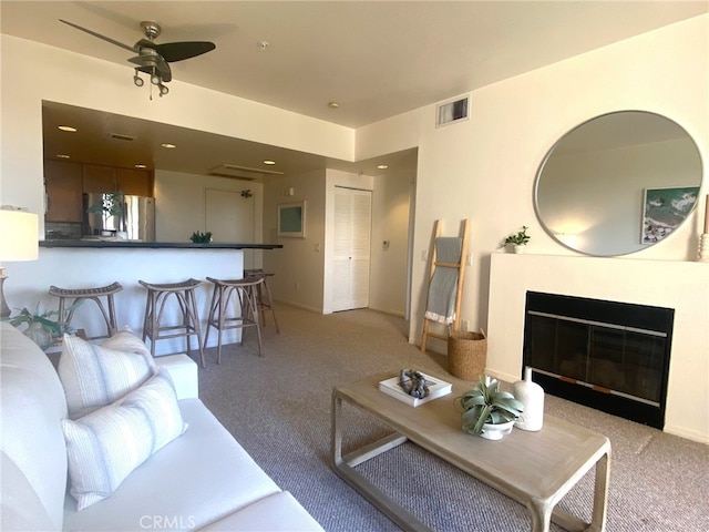 living area with a glass covered fireplace, a ceiling fan, visible vents, and carpet floors
