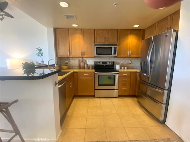 kitchen with visible vents, a sink, brown cabinets, stainless steel appliances, and decorative backsplash