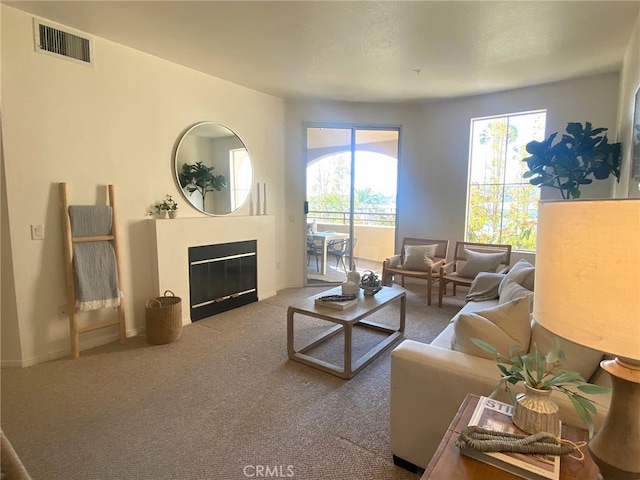 living room featuring carpet, a glass covered fireplace, visible vents, and a wealth of natural light