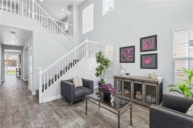 living area with stairway, a high ceiling, baseboards, and wood finished floors