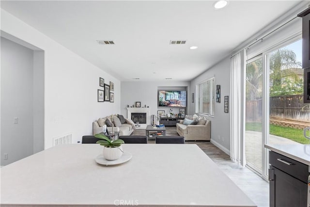 dining room featuring light wood finished floors, a glass covered fireplace, visible vents, and recessed lighting