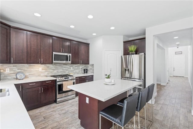 kitchen with light countertops, stainless steel appliances, backsplash, a kitchen island, and a breakfast bar area