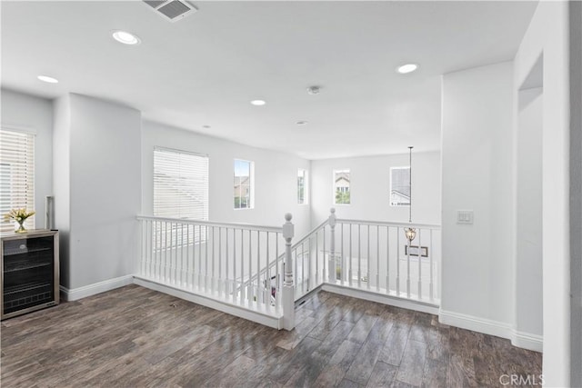 empty room featuring wood finished floors, baseboards, beverage cooler, and visible vents