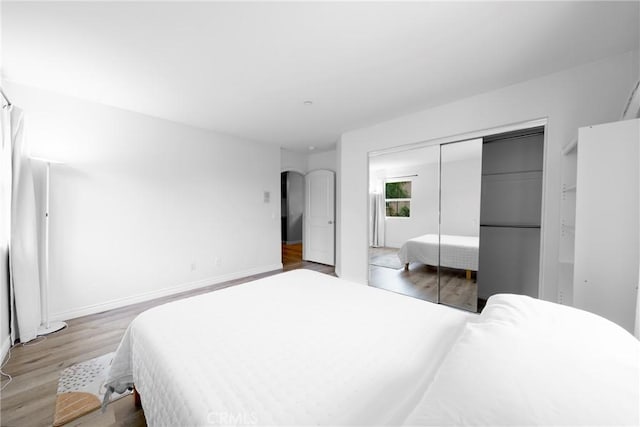 bedroom featuring baseboards, arched walkways, wood finished floors, and a closet