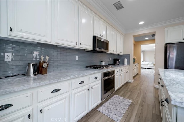 kitchen with crown molding, tasteful backsplash, stainless steel appliances, white cabinetry, and visible vents
