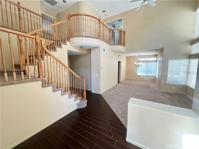 stairway with ceiling fan with notable chandelier, wood finished floors, a towering ceiling, and baseboards