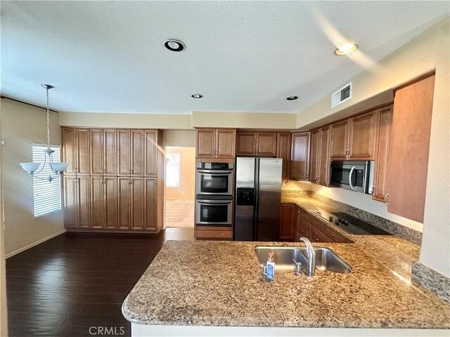 kitchen featuring a peninsula, visible vents, appliances with stainless steel finishes, light stone counters, and a sink