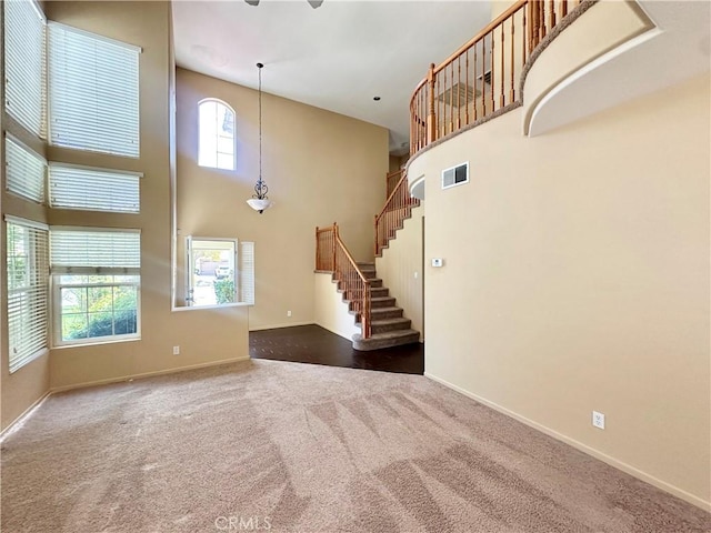 unfurnished living room featuring a towering ceiling, visible vents, baseboards, and dark carpet