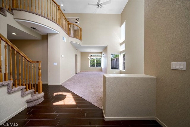 foyer with wood tiled floor, ceiling fan with notable chandelier, a towering ceiling, baseboards, and visible vents