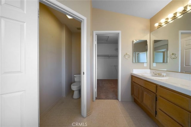 full bath with baseboards, toilet, a walk in closet, vanity, and tile patterned flooring