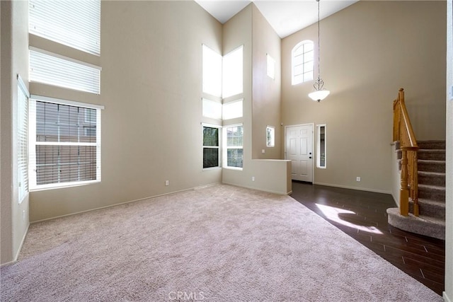 unfurnished living room with carpet floors, a high ceiling, baseboards, and stairs
