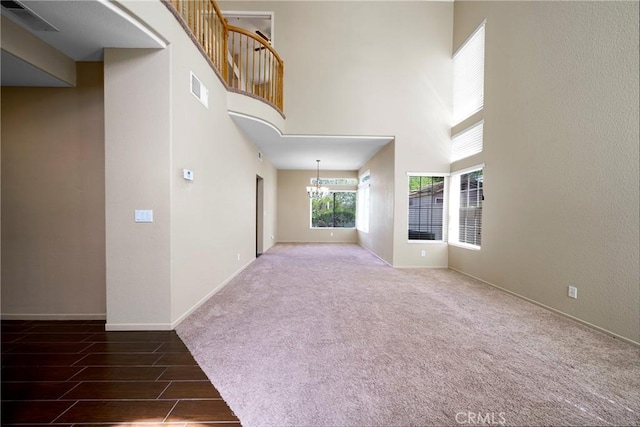 unfurnished living room with a chandelier, a high ceiling, baseboards, and visible vents
