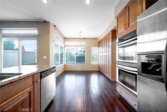 kitchen featuring brown cabinets, dark stone counters, baseboards, appliances with stainless steel finishes, and dark wood-style flooring