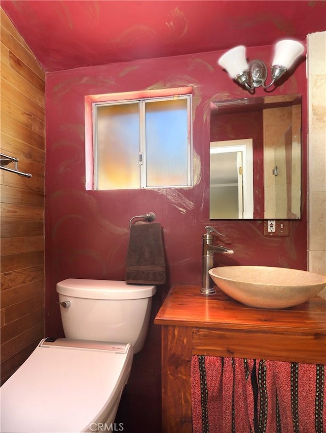 half bath with toilet, wooden walls, and a sink