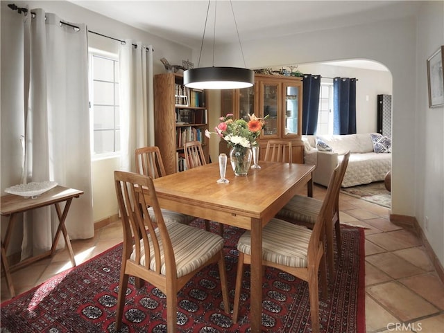 dining room with arched walkways, light tile patterned flooring, baseboards, and a wealth of natural light