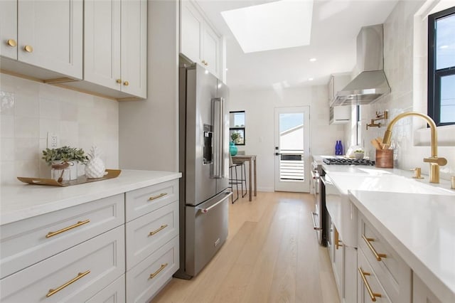 kitchen featuring high quality appliances, a skylight, decorative backsplash, light wood-style floors, and wall chimney exhaust hood