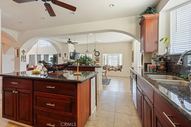 kitchen featuring ceiling fan, light tile patterned floors, arched walkways, a sink, and open floor plan