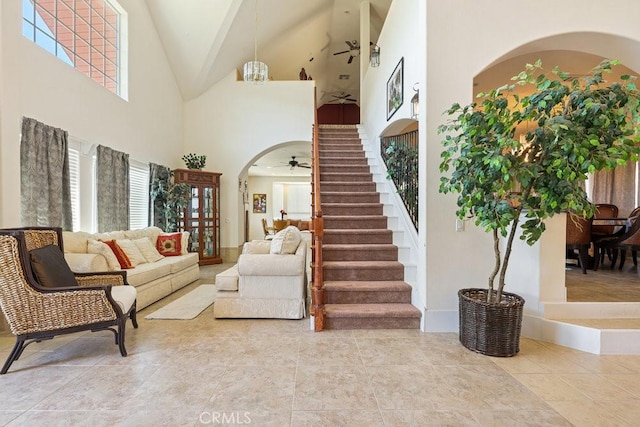 living area featuring arched walkways, high vaulted ceiling, a ceiling fan, and stairs