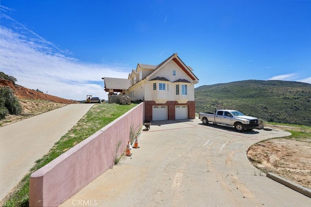 exterior space with a garage, stucco siding, fence, a mountain view, and concrete driveway