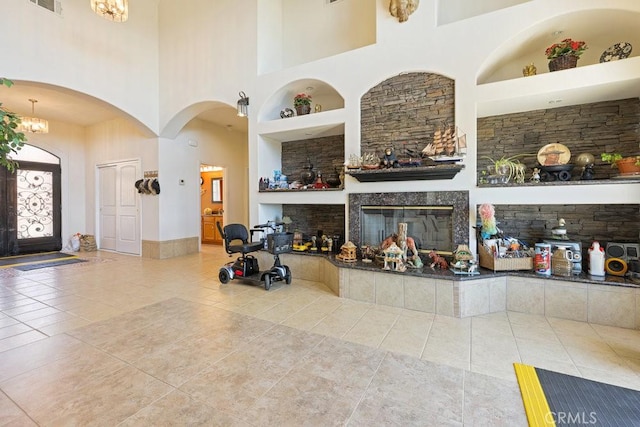unfurnished living room with a towering ceiling, tile patterned flooring, visible vents, arched walkways, and built in shelves