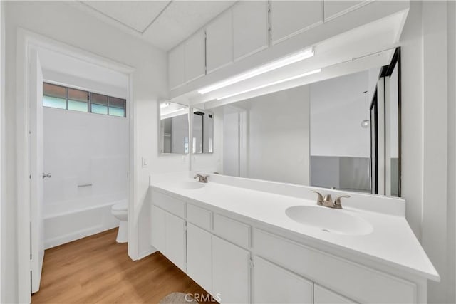 bathroom featuring toilet, wood finished floors, double vanity, and a sink