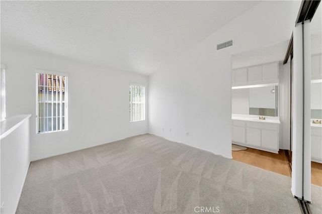 unfurnished bedroom featuring vaulted ceiling, ensuite bathroom, visible vents, and carpet