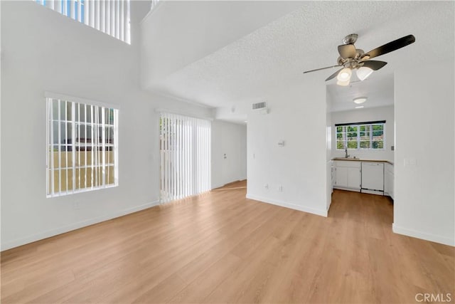 unfurnished living room with baseboards, light wood-style flooring, a textured ceiling, visible vents, and ceiling fan