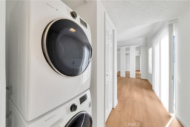 laundry area featuring light wood-style floors, a textured ceiling, stacked washer / dryer, and laundry area