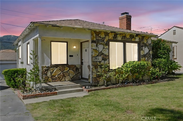 view of front of property featuring a front yard, stucco siding, stone siding, and a chimney