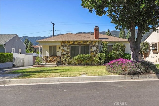 view of front of house featuring a front yard, stone siding, a chimney, fence, and stucco siding