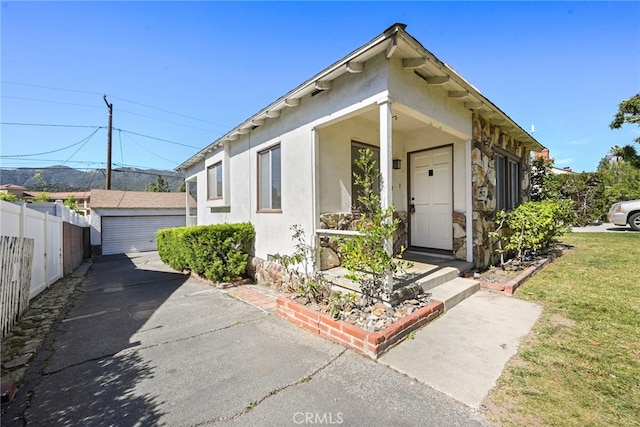 view of front of house featuring an outbuilding, a detached garage, stucco siding, fence, and a front lawn
