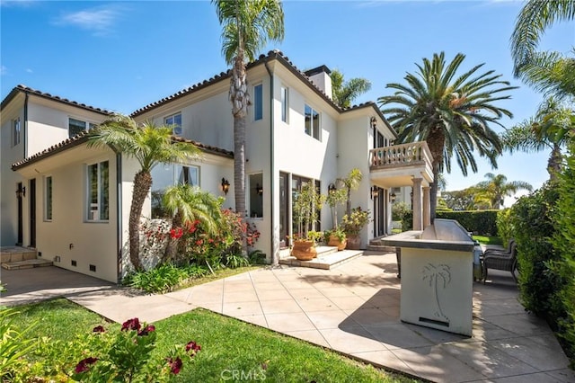 rear view of house featuring a patio, a chimney, stucco siding, and a balcony