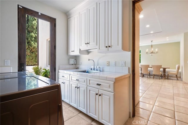 kitchen with light tile patterned floors, white cabinets, an inviting chandelier, a sink, and tile counters