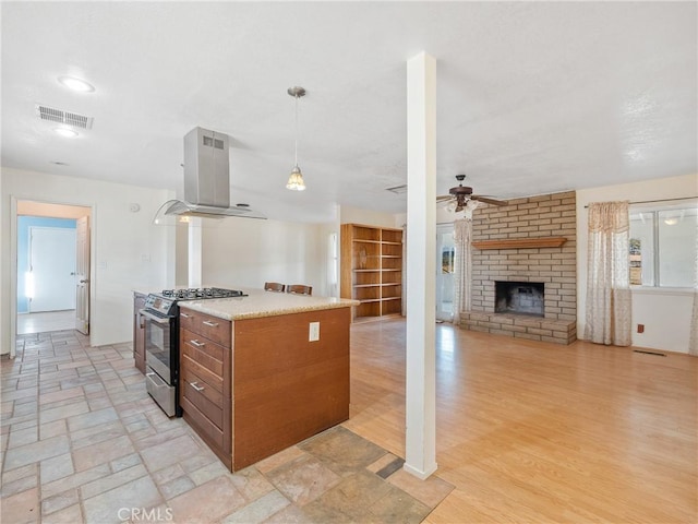 14435 Hopi Rd, Apple Valley, CA 92307 - kitchen featuring stainless steel range with gas cooktop, visible vents, a brick fireplace, island range hood, and a ceiling fan