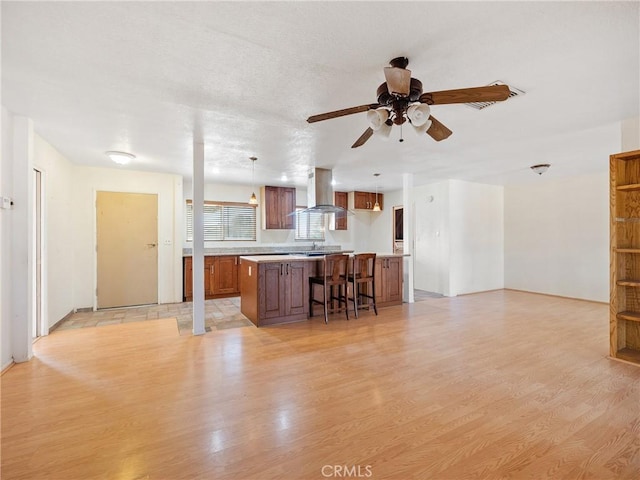 14435 Hopi Rd, Apple Valley, CA 92307 - kitchen featuring brown cabinetry, wall chimney exhaust hood, light wood-style flooring, light countertops, and a kitchen island