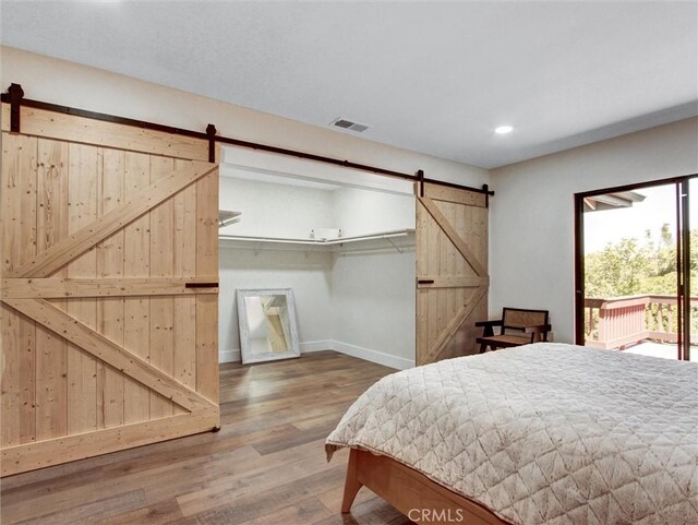 bedroom with access to outside, recessed lighting, a barn door, wood finished floors, and baseboards