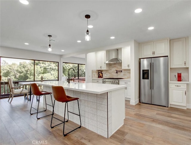 kitchen with light countertops, light wood-type flooring, wall chimney exhaust hood, and stainless steel fridge