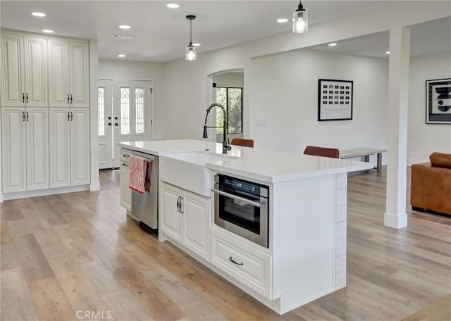 kitchen featuring light countertops, decorative light fixtures, light wood-style floors, appliances with stainless steel finishes, and arched walkways