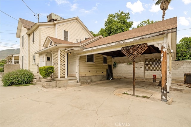 rear view of property featuring fence, a chimney, a carport, and a shingled roof