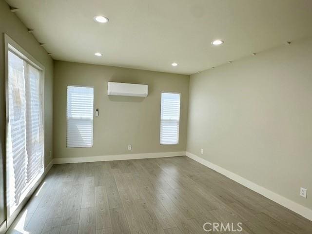 empty room with a wall mounted air conditioner, baseboards, wood finished floors, and recessed lighting