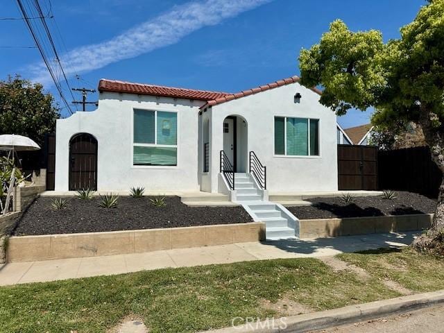 mediterranean / spanish home with stucco siding, fence, and a tiled roof